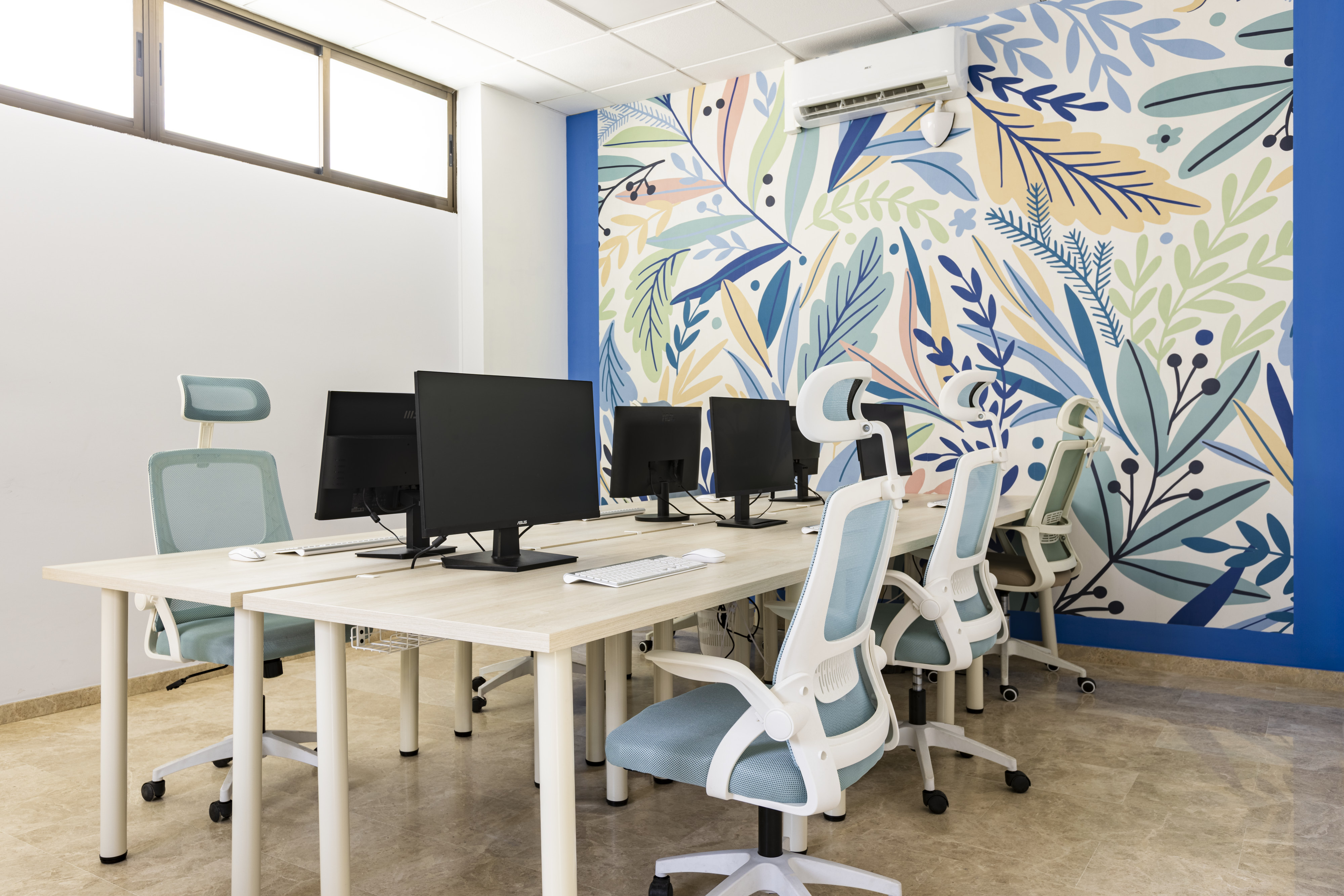 Puestos de trabajo con monitores y sillas ergonómicas frente a un mural botánico